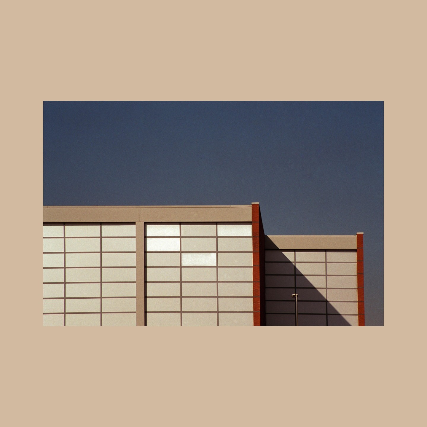 A modern building with a grid of windows and a brick facade is partially covered in shadow under a dark blue sky.