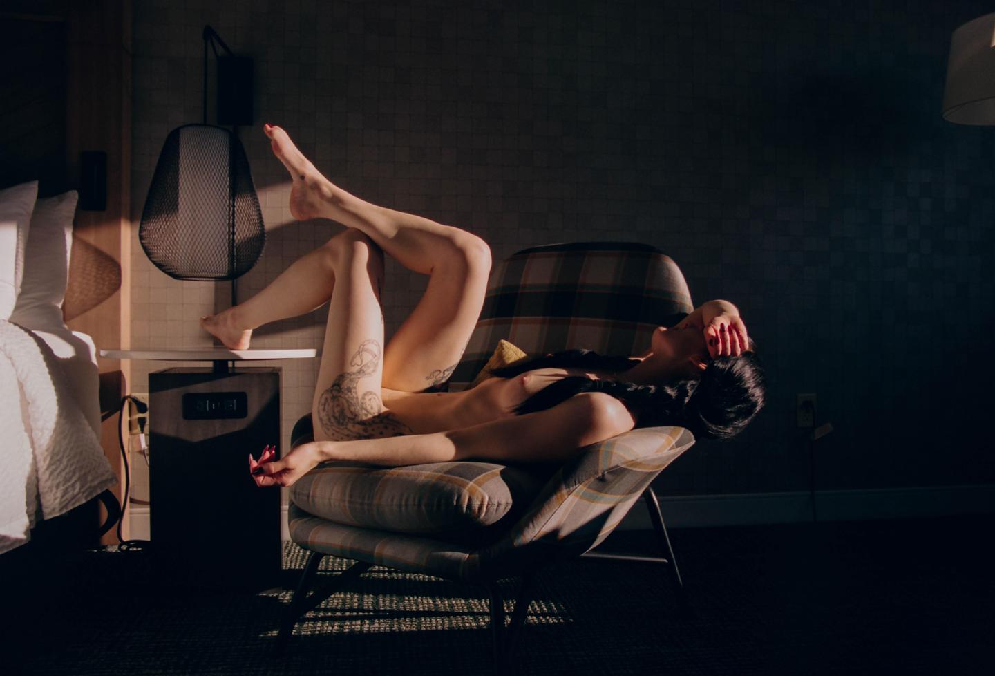 A woman reclines on a plaid armchair with her legs up and her arm over her face, illuminated by a shaft of light.
