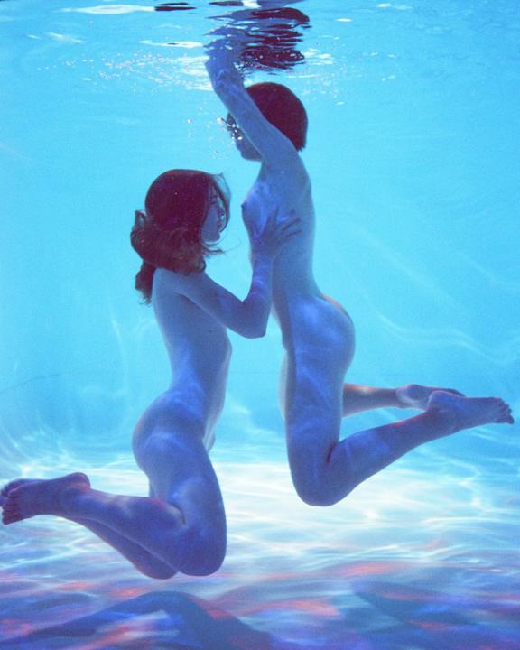 Two women with red hair are underwater, one holding the other around the waist.