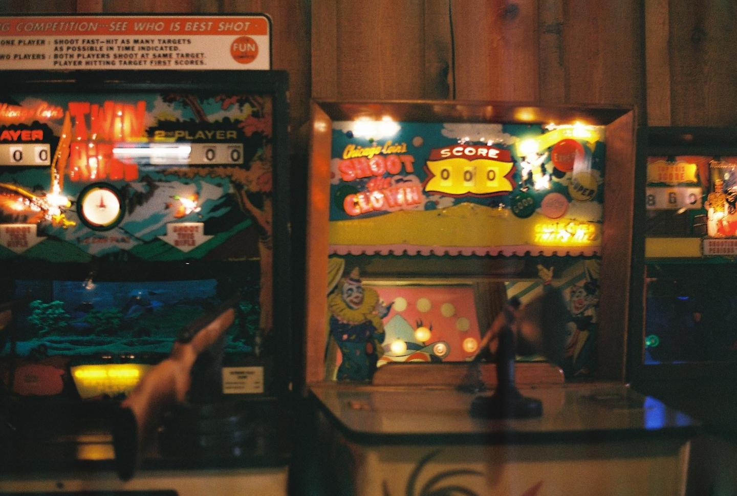 Three arcade games with bright lights are lined up against a wooden wall.
