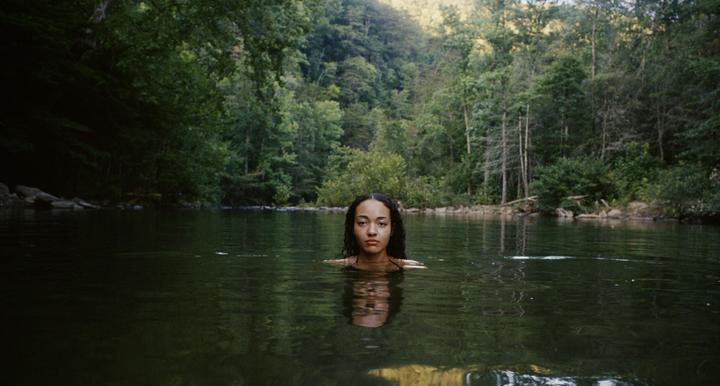 A woman is swimming in a body of water surrounded by a dense forest.