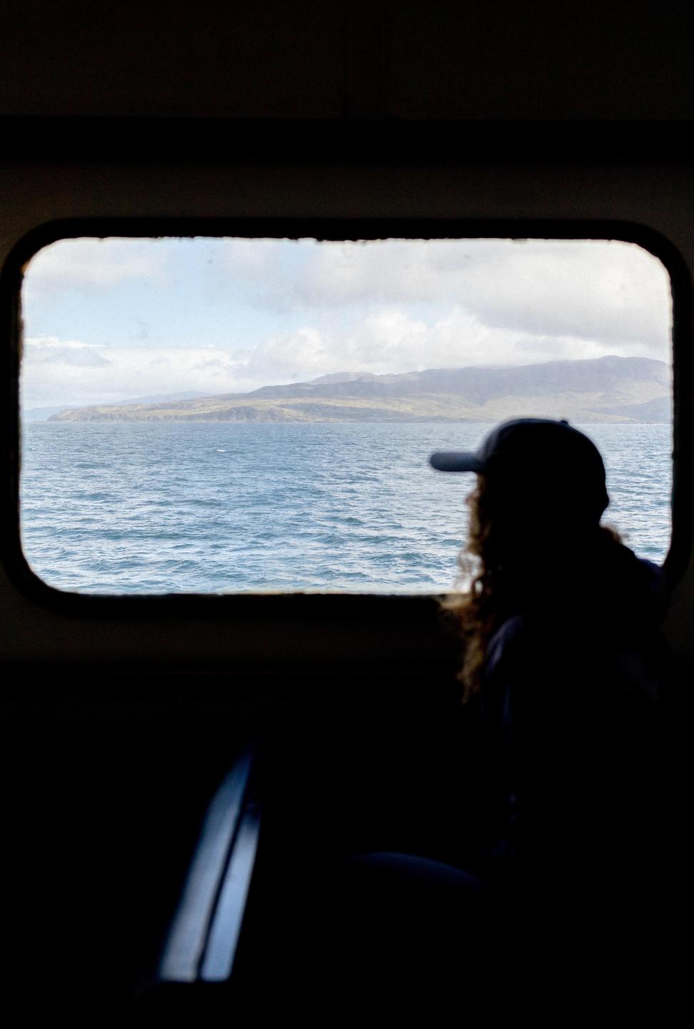 A person in silhouette looks out a window at a body of water and distant land.