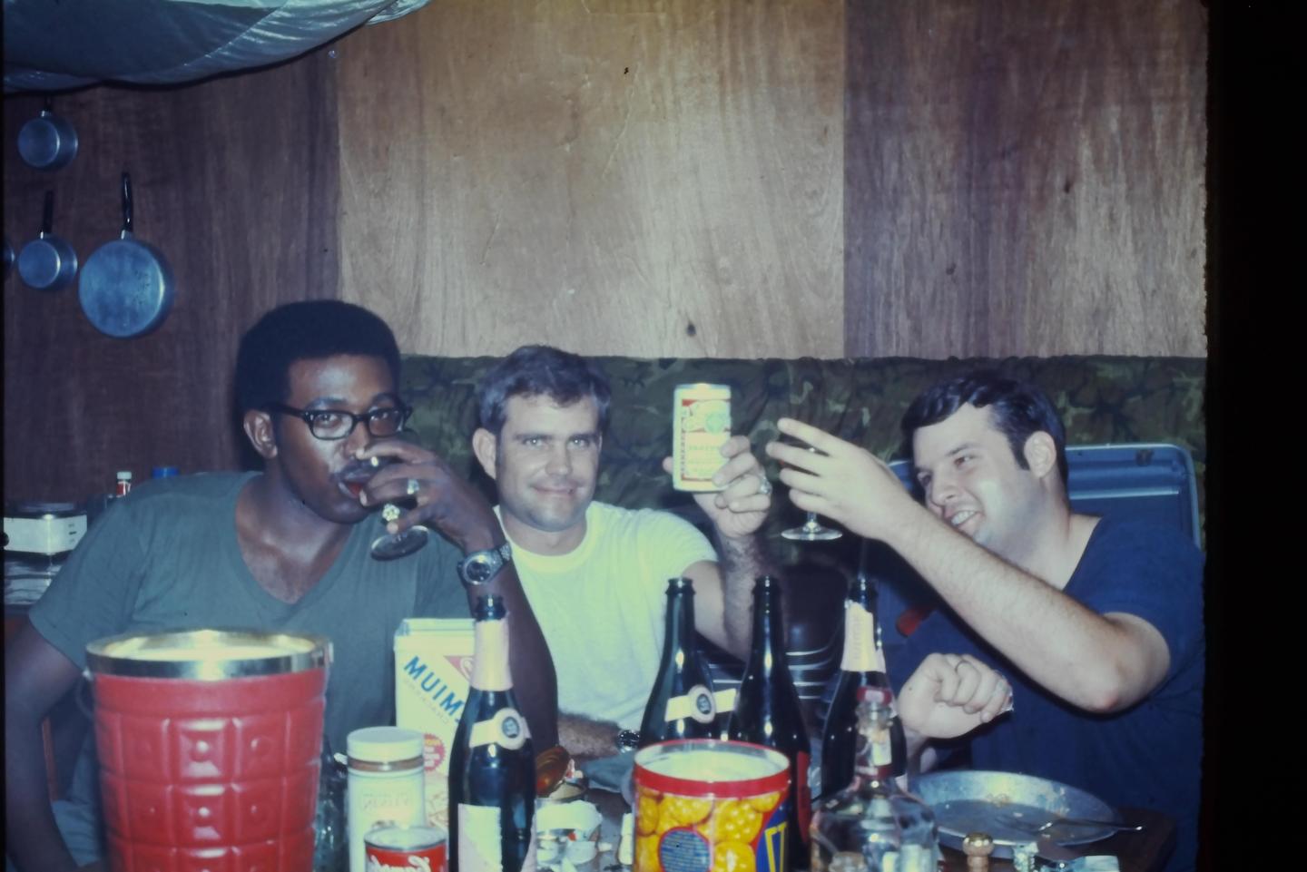 Three men are sitting around a table with drinks and bottles.