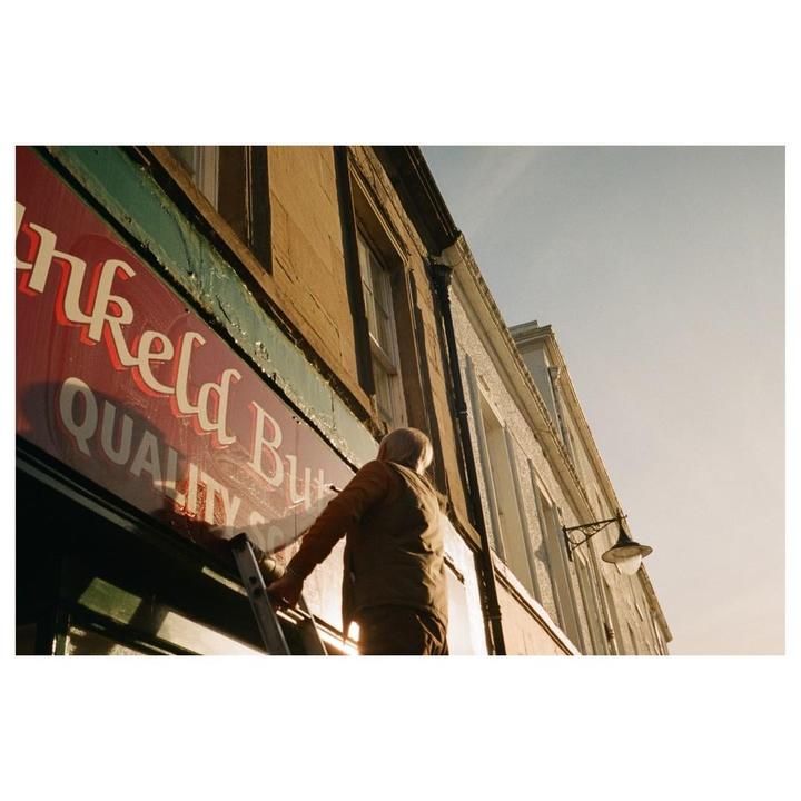 A man on a ladder cleans a red sign on the side of a building.