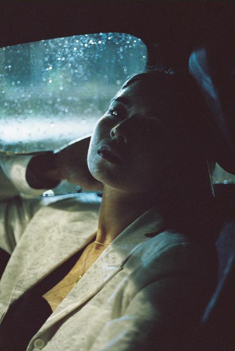 A woman sits in a car at night, looking up at the rain-streaked window.