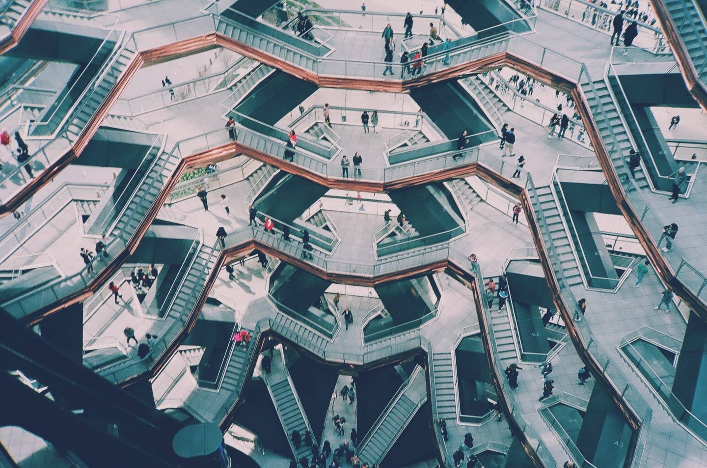 A high-angle view shows many people walking on the intricate staircases and platforms of a modern building.