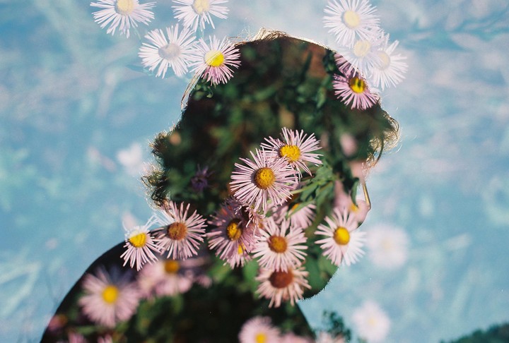 A double exposure shows the silhouette of a person's head filled with flowers, superimposed over a light blue background with more flowers.