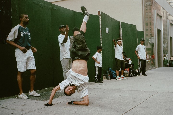 A man performs a handstand on a city sidewalk while other men watch.