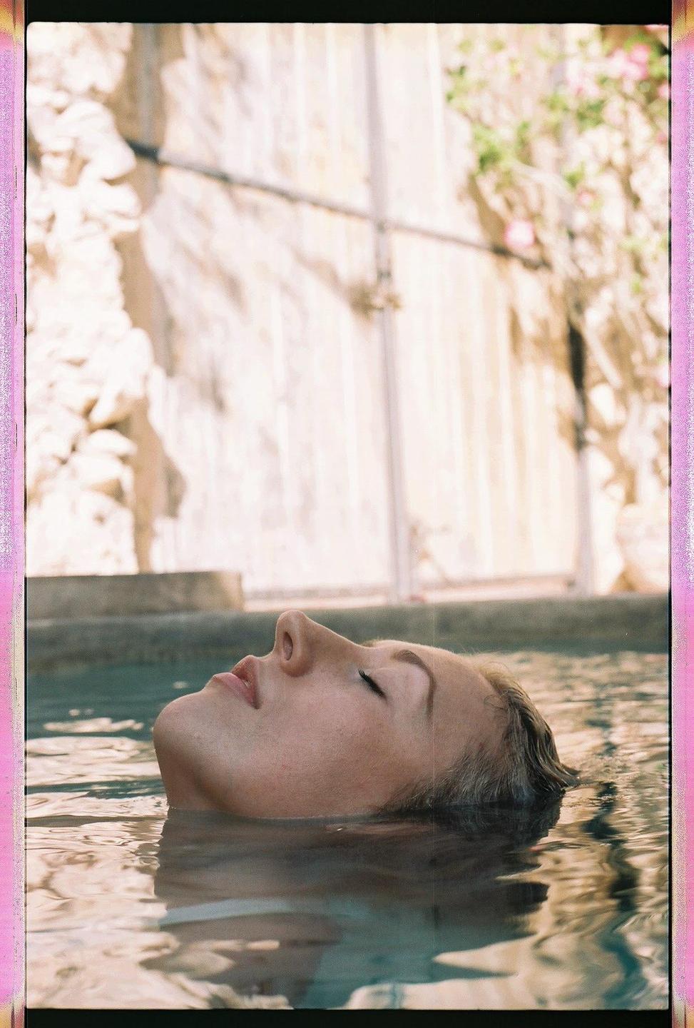 A woman floats on her back in water with her eyes closed and her face looking up.