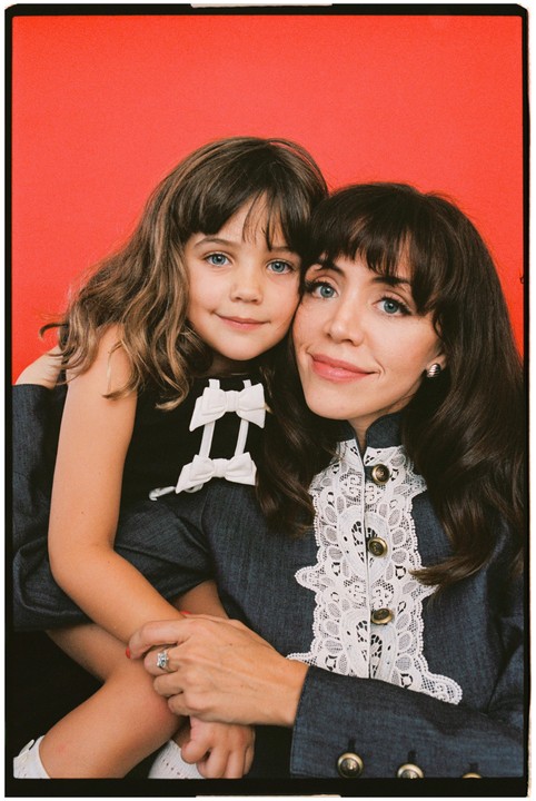 A woman and a girl pose for a portrait against a red background.