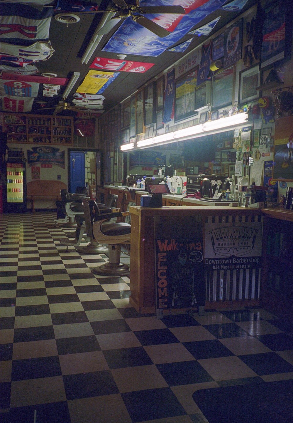 A barbershop with a checkered floor and several barber chairs is illuminated by fluorescent lights.
