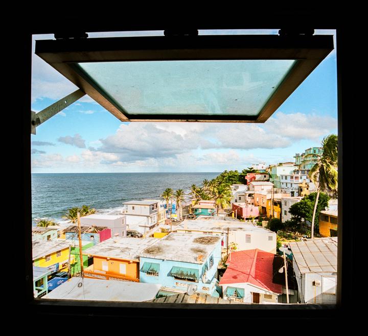A view of a colorful coastal town and the ocean through an open window.