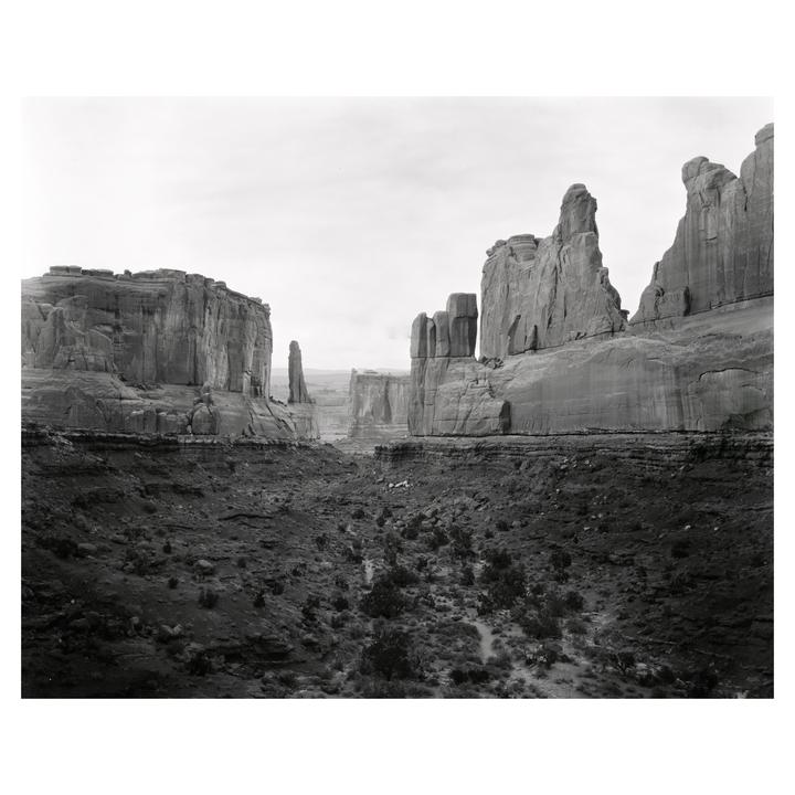A black and white landscape shows a valley between tall rock formations under a bright sky.