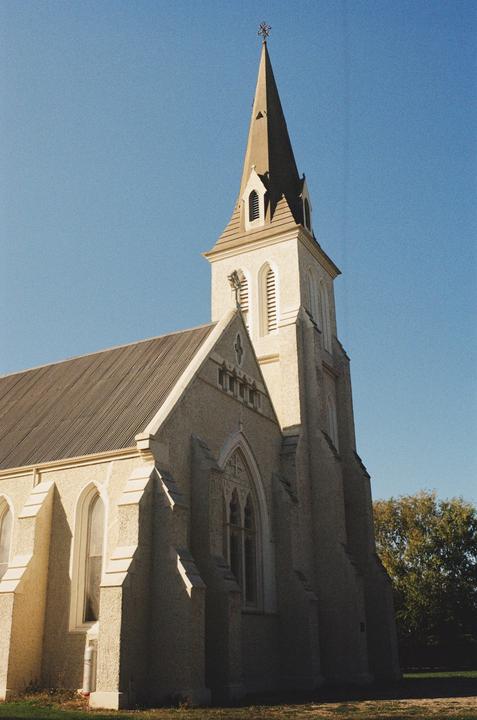 A church with a tall steeple stands against a clear blue sky.