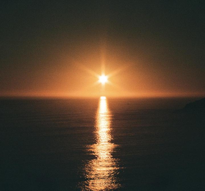 The sun sets over the ocean, creating a bright reflection on the water.