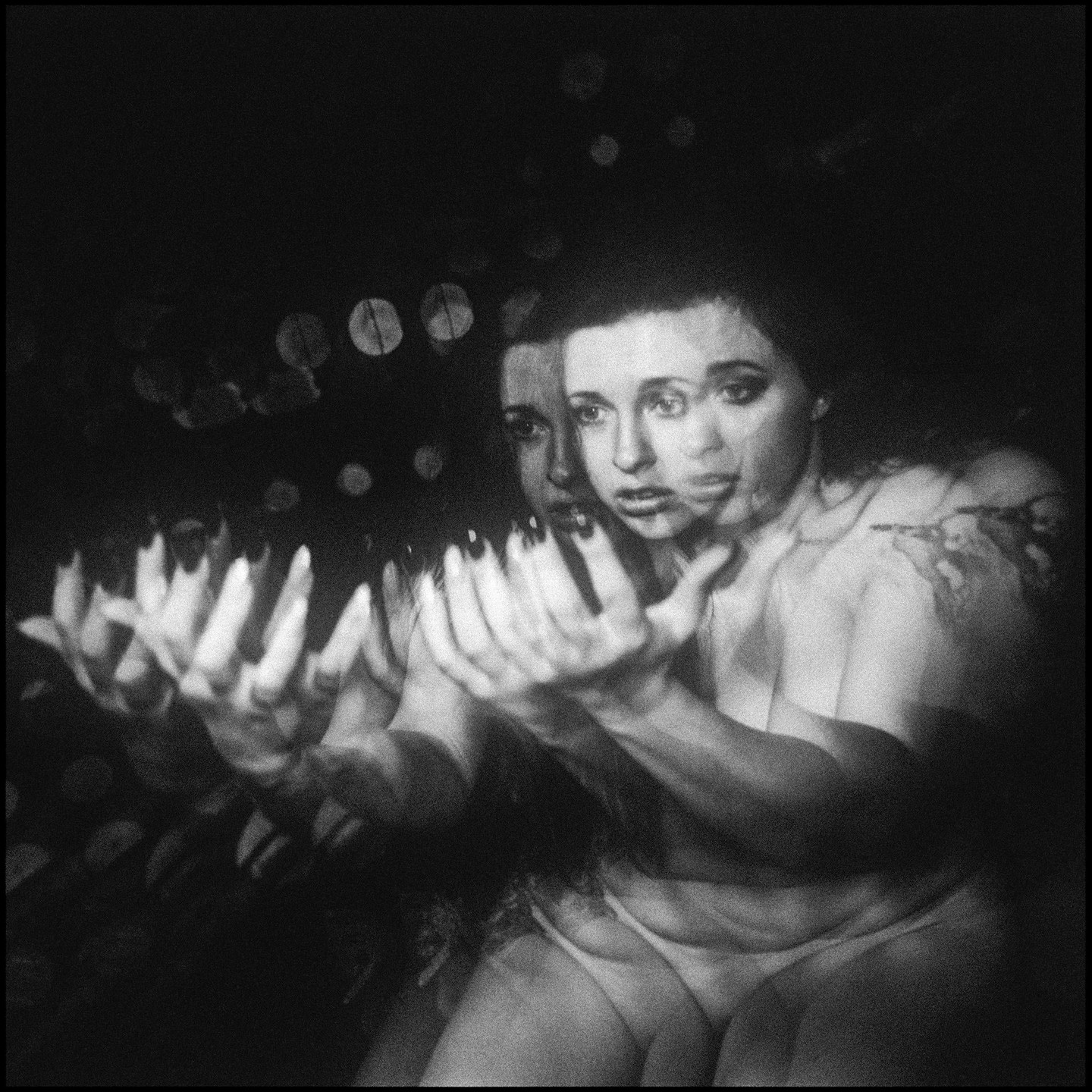 A woman with multiple exposures holds her hands out in front of her.