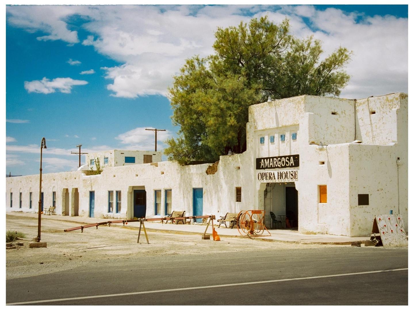 A white building with "Amargosa Opera House" written on it stands under a blue sky with clouds.