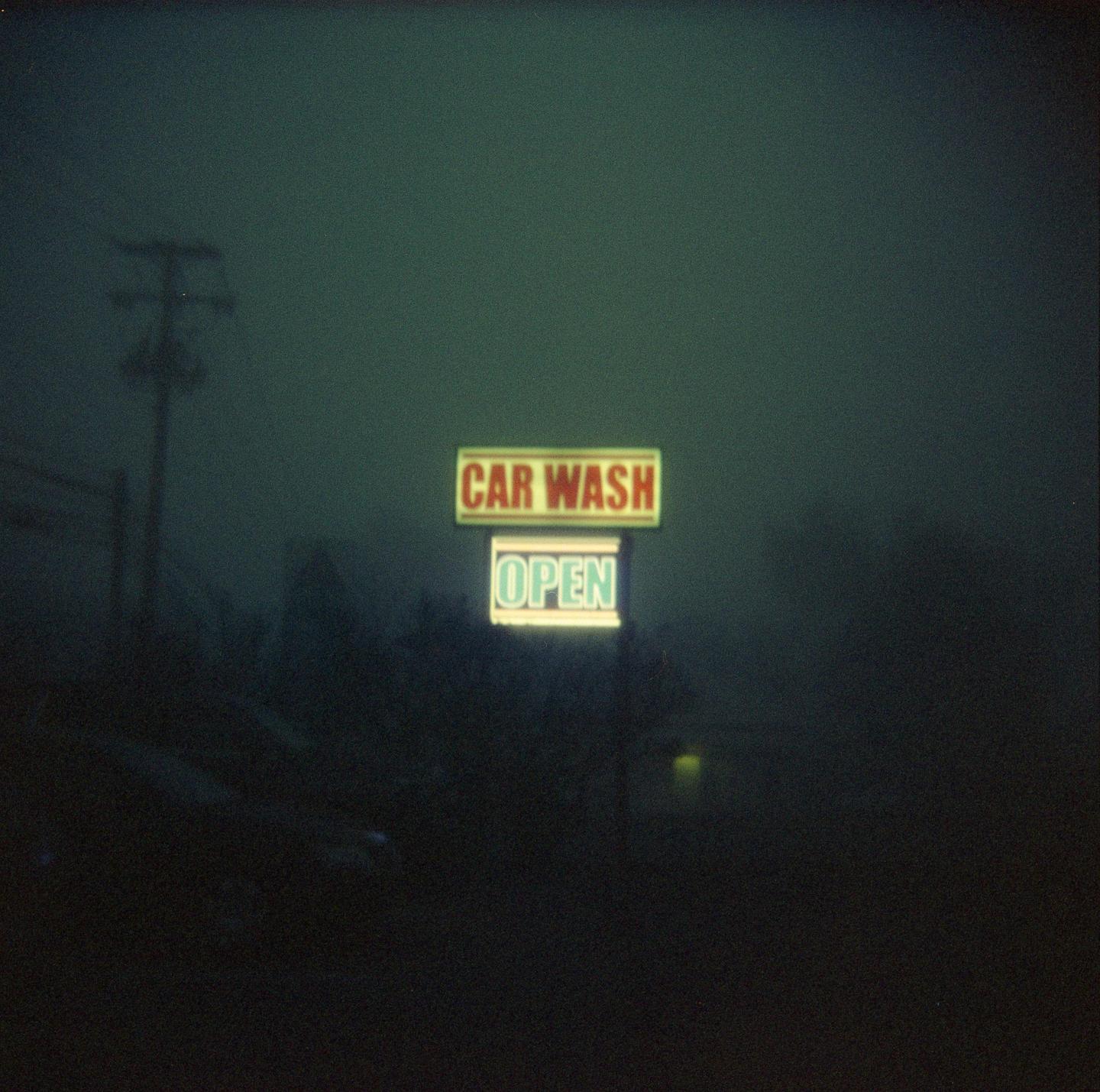 A neon sign for a car wash that says "OPEN" is visible through a thick fog at night.