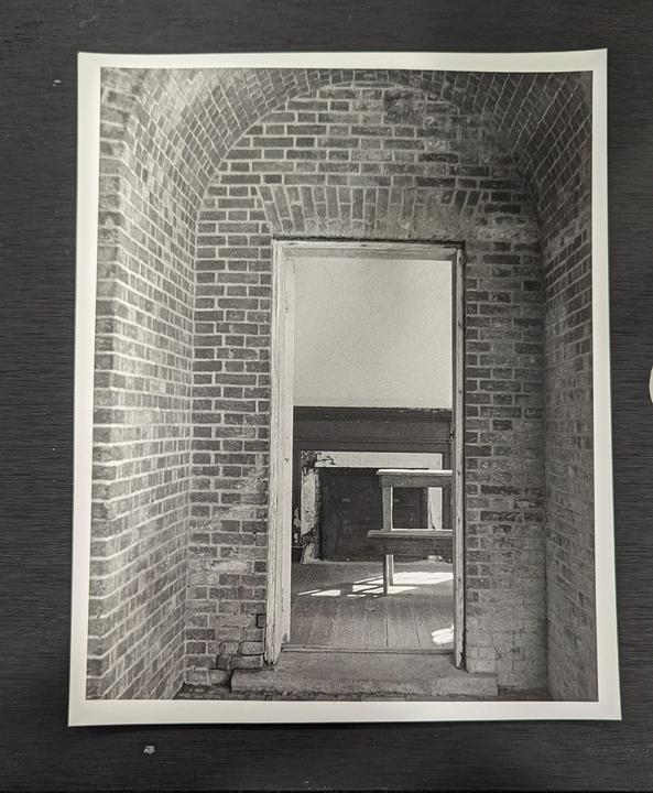 A brick archway leads to a room with a wooden floor and a table.