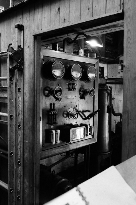 A control panel with gauges and switches is illuminated by a lamp in a generator room.