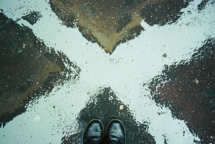 A pair of black boots stands on wet asphalt with a white X painted on it.