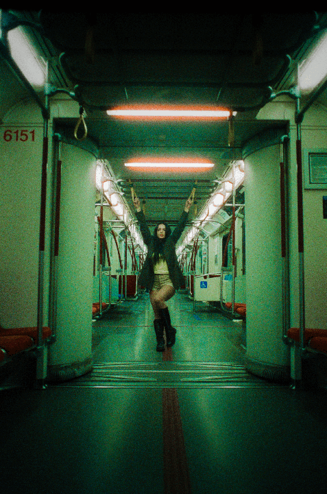 A woman stands in the middle of an empty subway car with her arms raised.