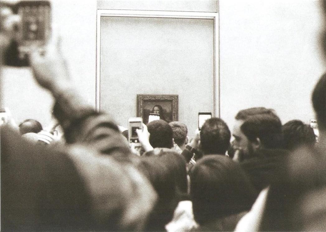 A crowd of people photograph the Mona Lisa painting in a museum.