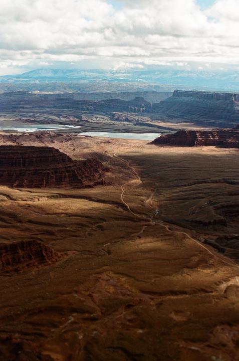 A vast canyon landscape with a river and mountains in the distance is visible under a cloudy sky.