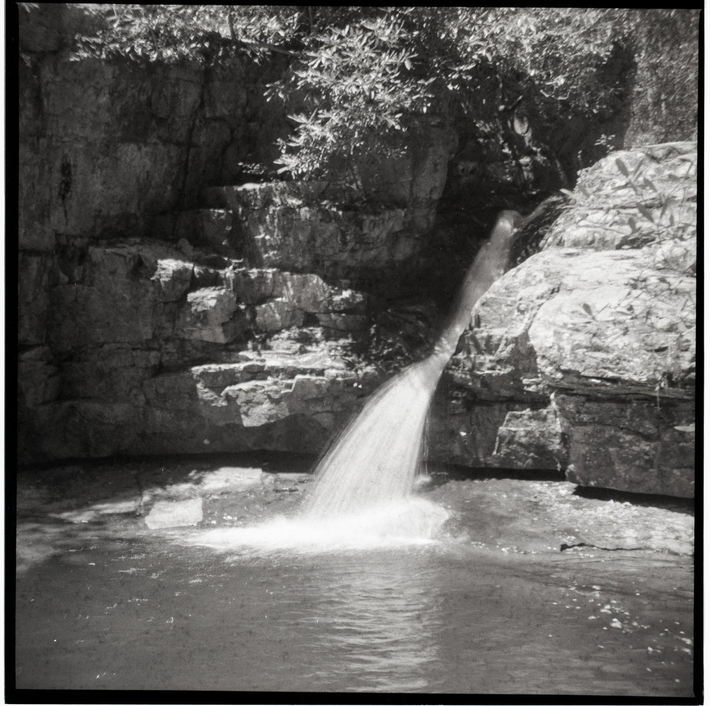 A waterfall cascades into a pool of water surrounded by rocky cliffs and foliage.