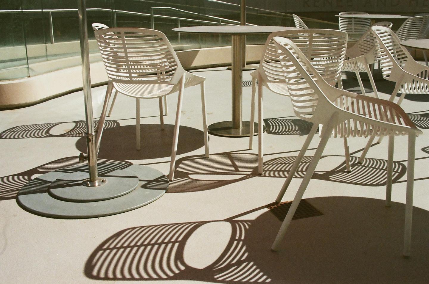 White chairs and tables cast striped shadows on a patio.