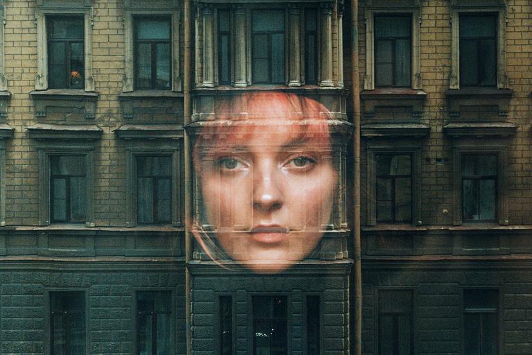 A woman's face is superimposed over the facade of a brick building with many windows.