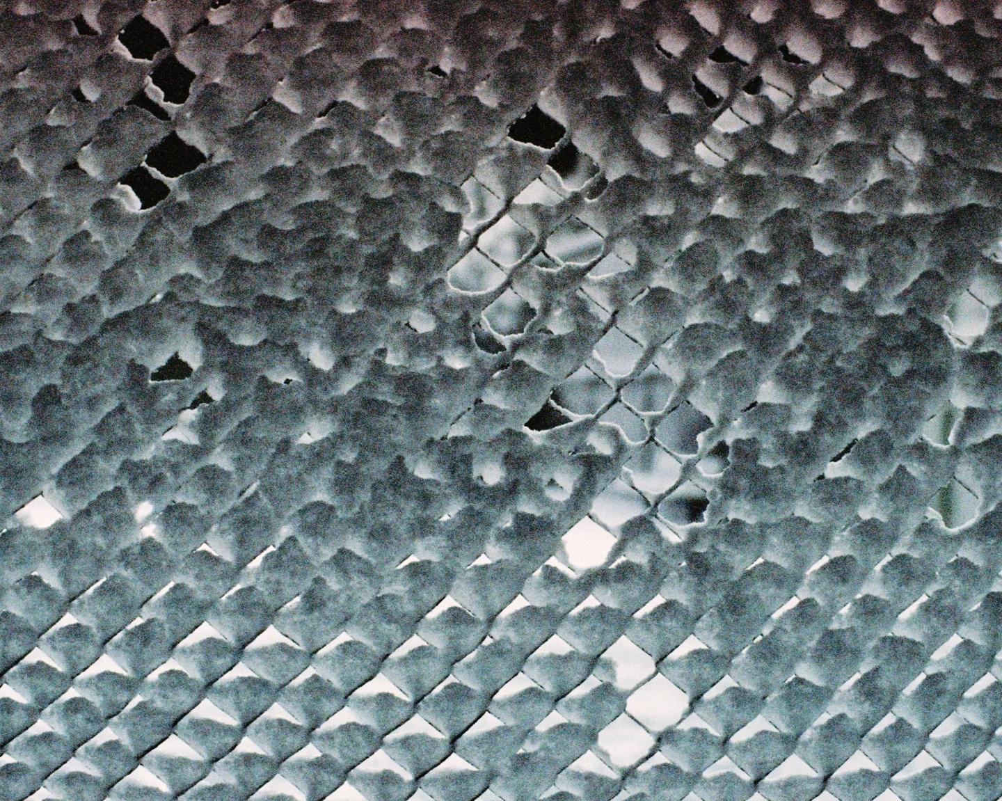 A chain link fence is covered in a fresh layer of snow.