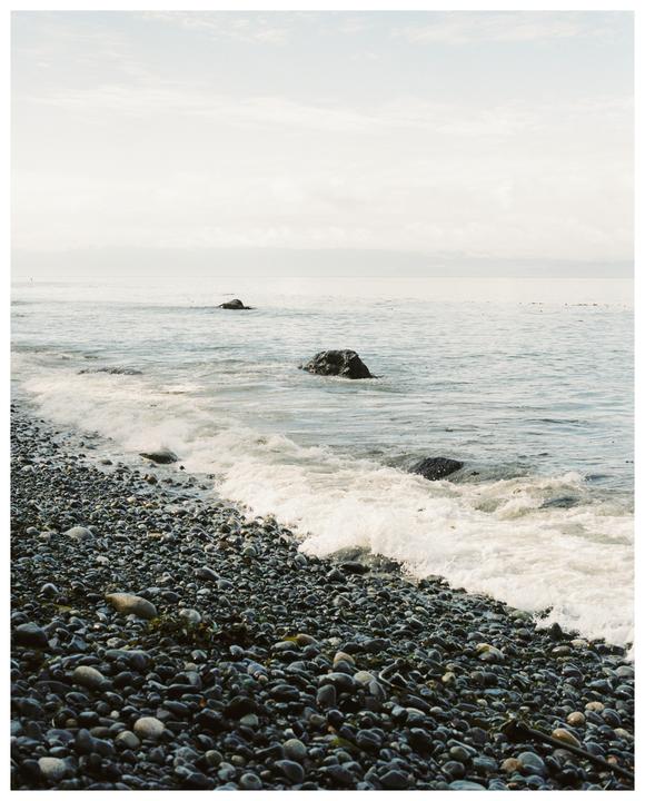 Waves crash on a rocky beach with two large rocks visible in the water.