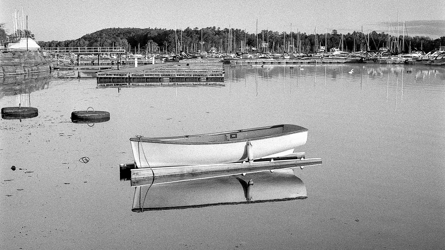 A small boat is moored in a marina with many sailboats and docks in the background.