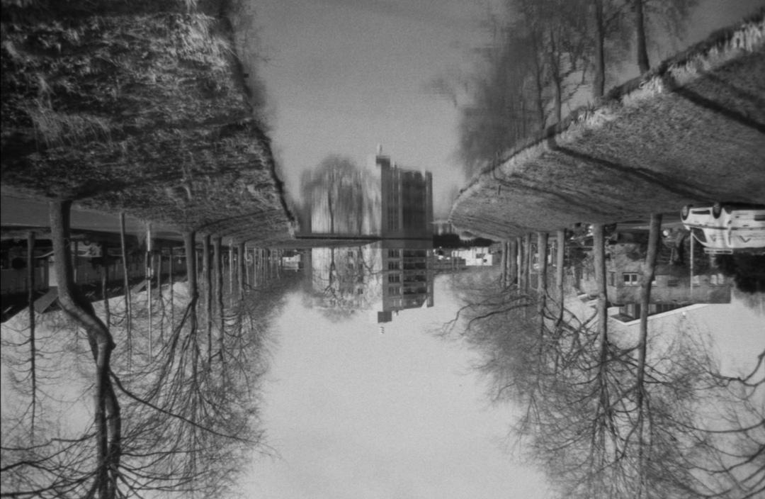 A black and white photo shows a canal with trees and buildings on either side, with the image inverted.