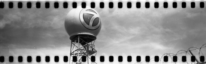 A large spherical structure with a number seven logo is mounted on a metal tower, with barbed wire in the foreground.