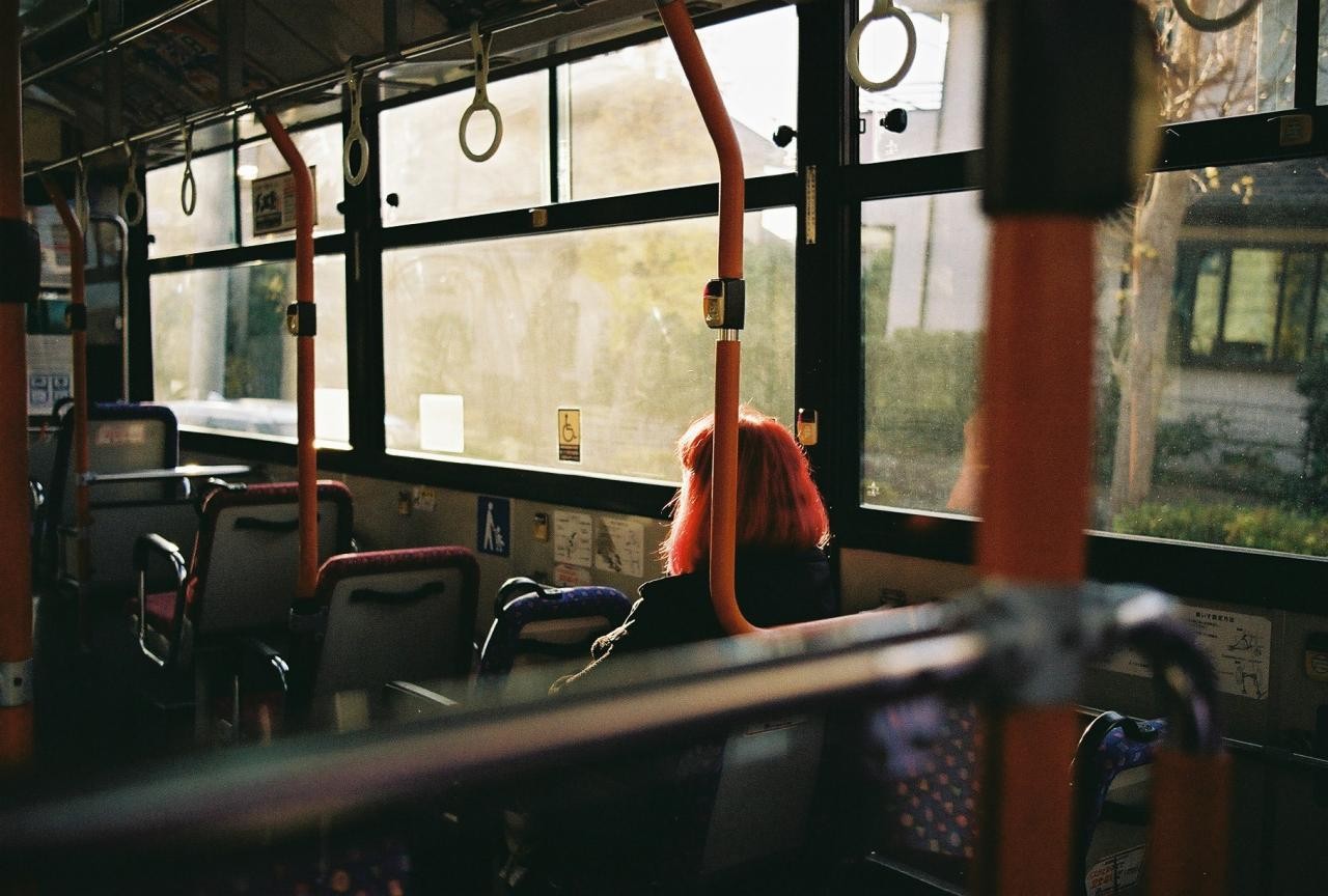 A person with bright red hair sits on a bus looking out the window.
