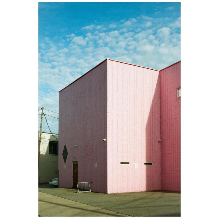 A pink building with a dark shadow on one side stands under a blue sky with white clouds.