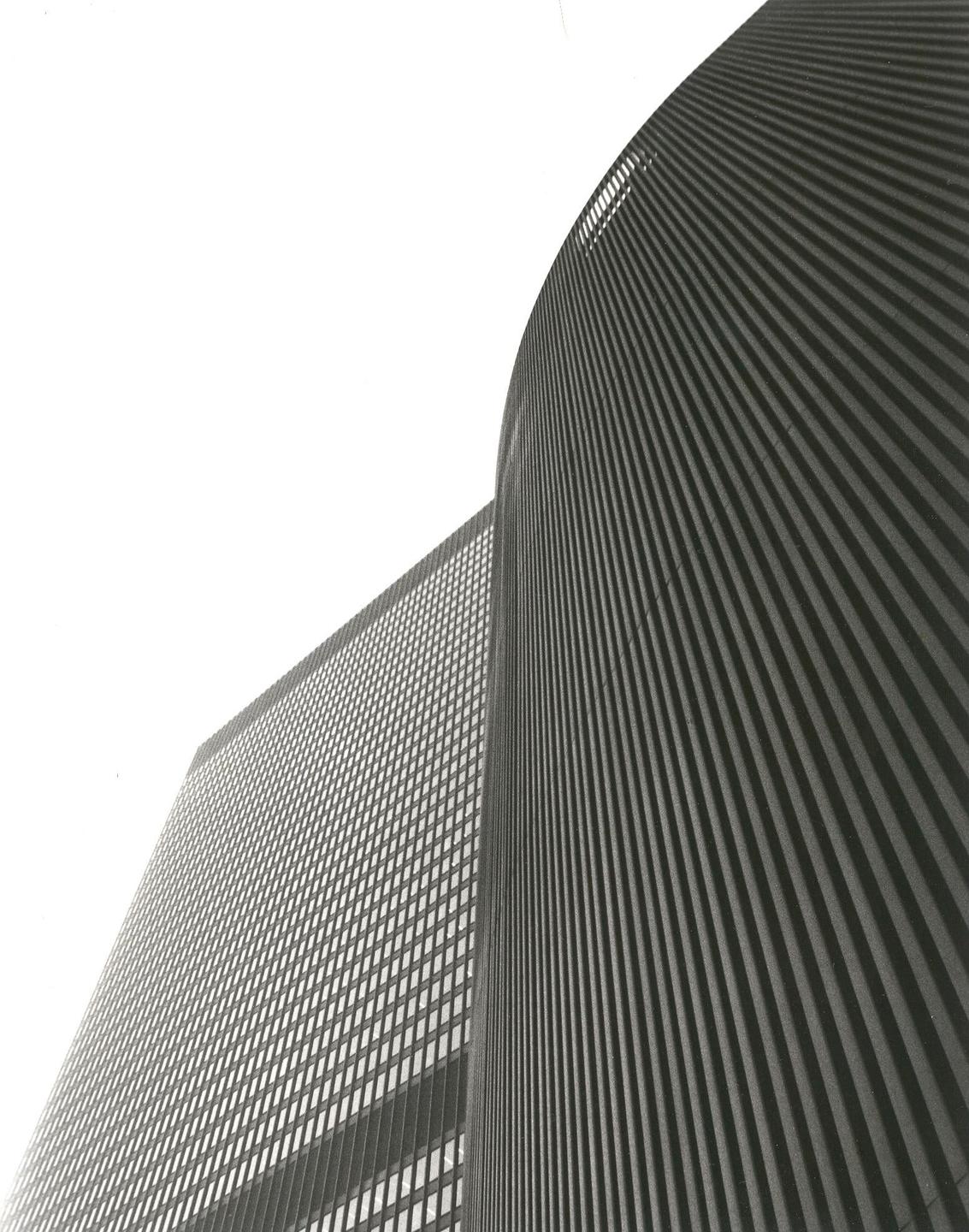 Two tall buildings with textured facades are seen from a low angle against a bright sky.