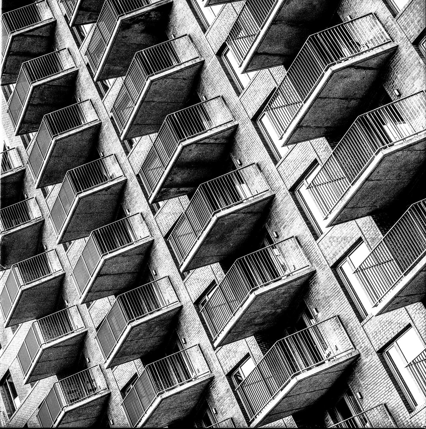 A black and white photograph shows a repeating pattern of balconies on a building.
