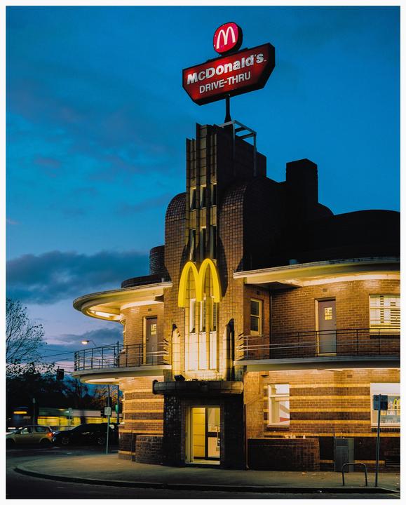 A McDonald's restaurant with an Art Deco design is illuminated at dusk.