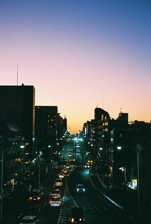 A long exposure shot captures the light trails of cars on a city street at dusk, with buildings silhouetted against the colorful sky.