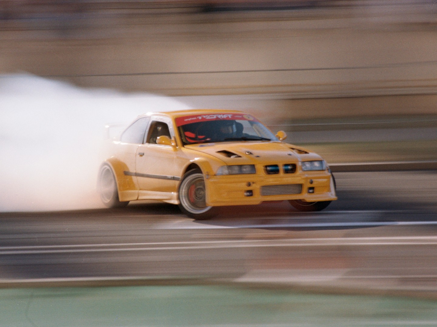 A yellow race car drifts on a track, creating a large cloud of smoke from its tires.