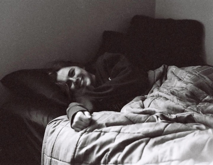 A woman lies in bed, smiling, with a blanket covering her body.
