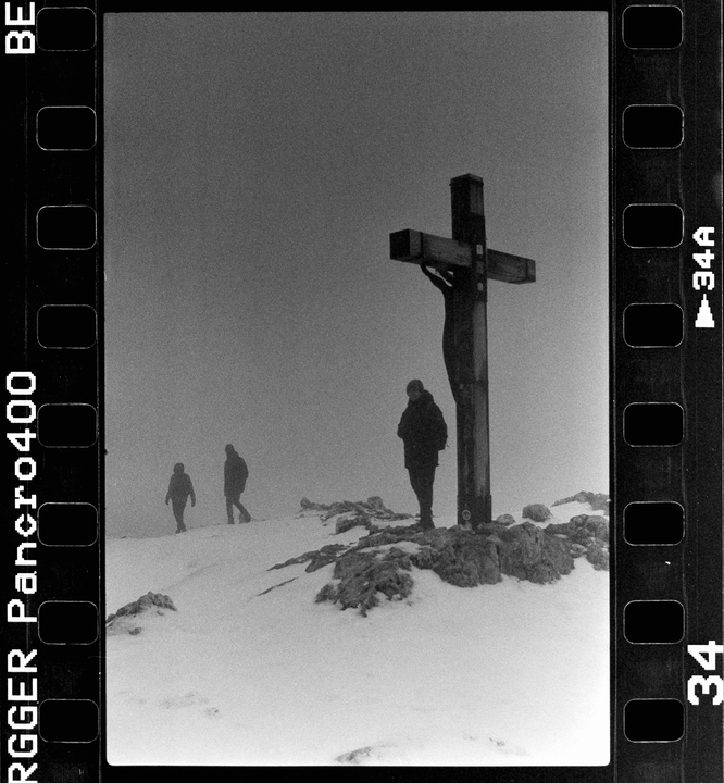 Three people stand in a snowy, rocky landscape next to a large crucifix.