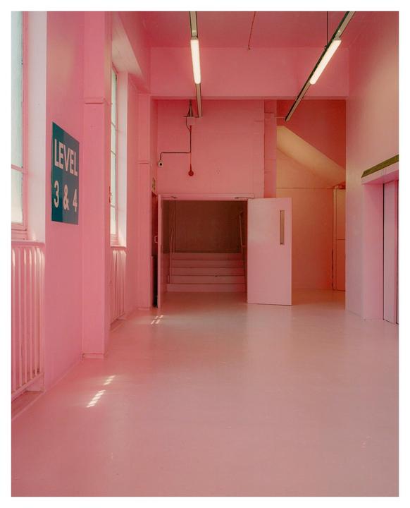 A hallway with pink walls and floor leads to a staircase and an open door.