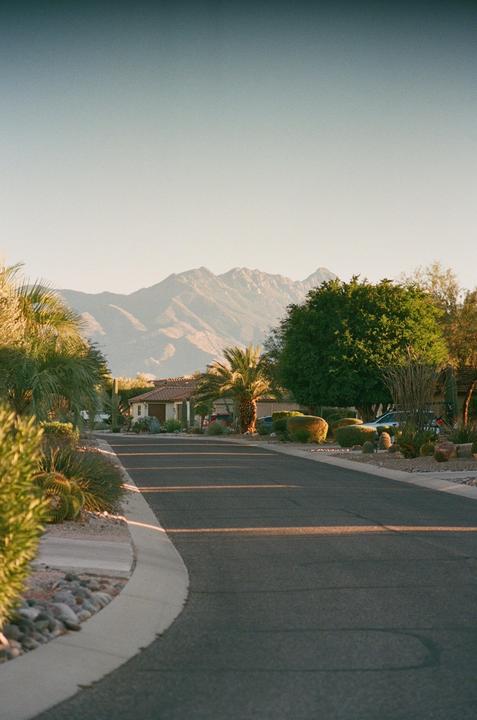 A paved road curves through a residential neighborhood with mountains in the background.