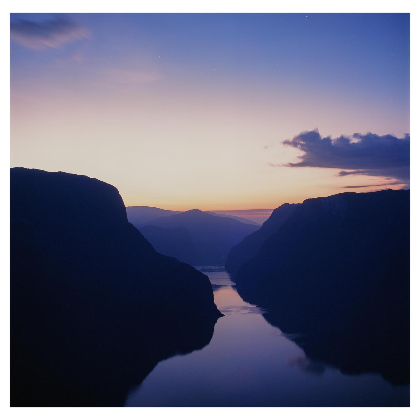 A body of water reflects the sky between two mountains at dusk.