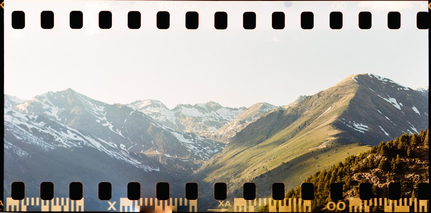 A mountain range with patches of snow and green slopes is visible under a bright sky.