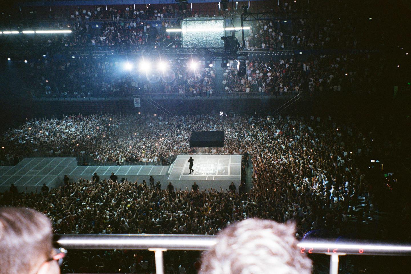 A performer stands on a stage surrounded by a large crowd at a night concert.